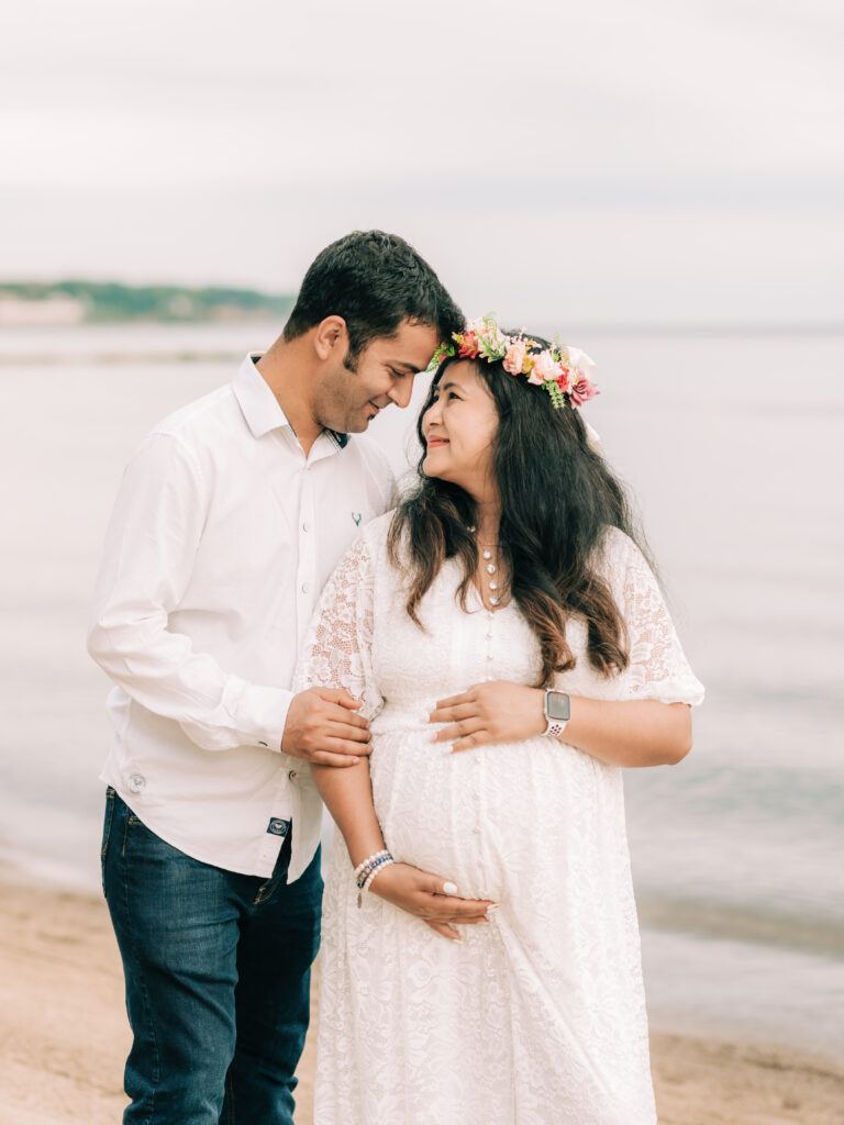 husband and wife holding pregnant belly for beach maternity photoshoot Huntington Beach Bay Village