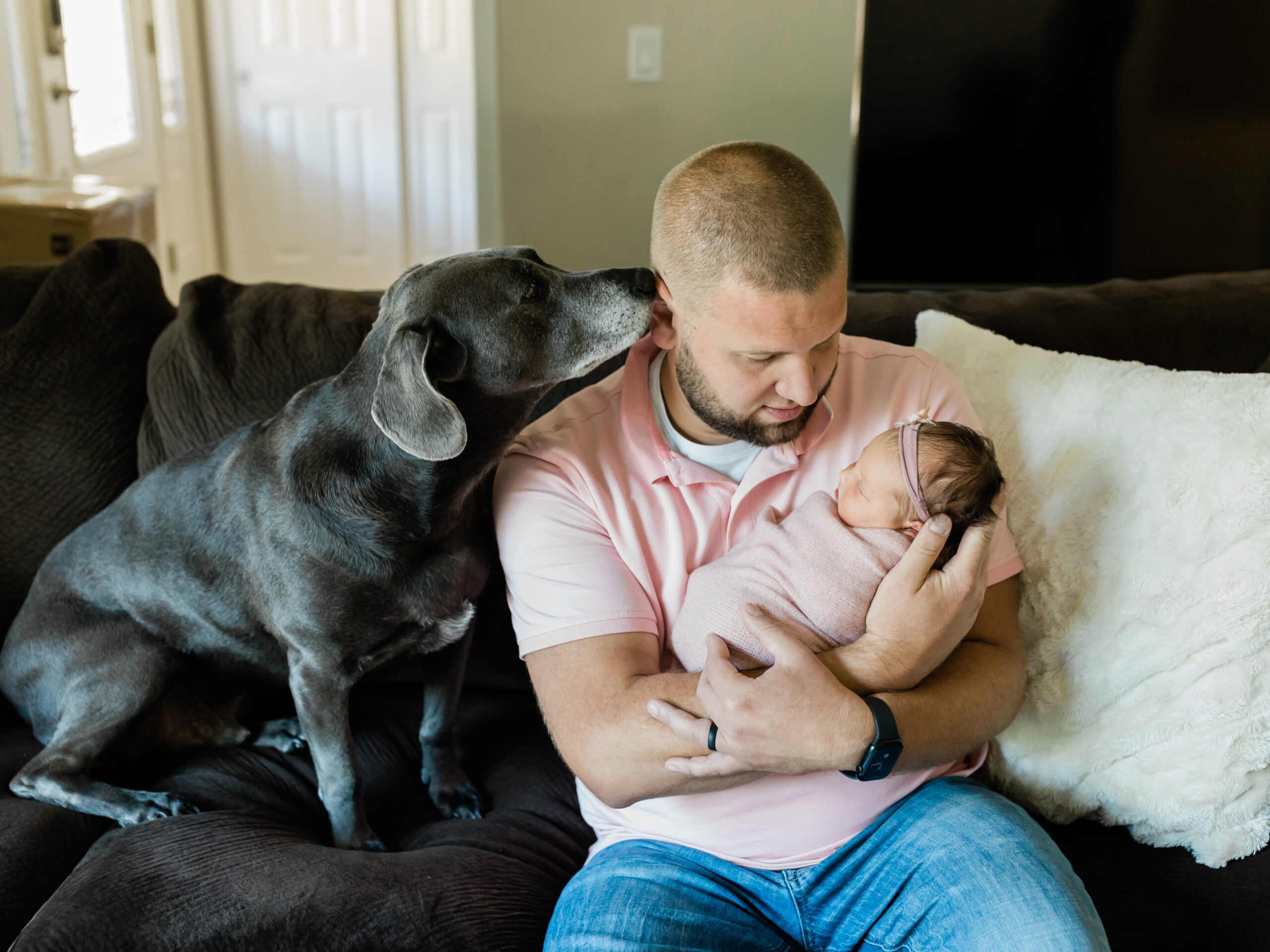 dad holding newborn baby girl sitting next to dog