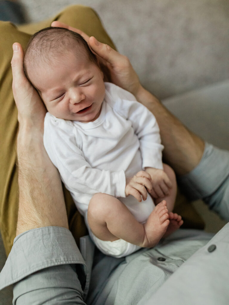 dad holding newborn baby boy in lap for photoshoot