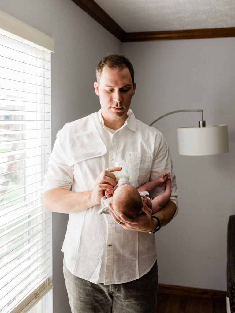 dad feeding newborn baby girl bottle during in home photoshoot