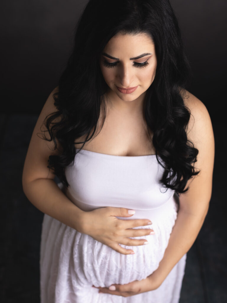 pregnant mom holding belly for maternity photos wearing lace white dress