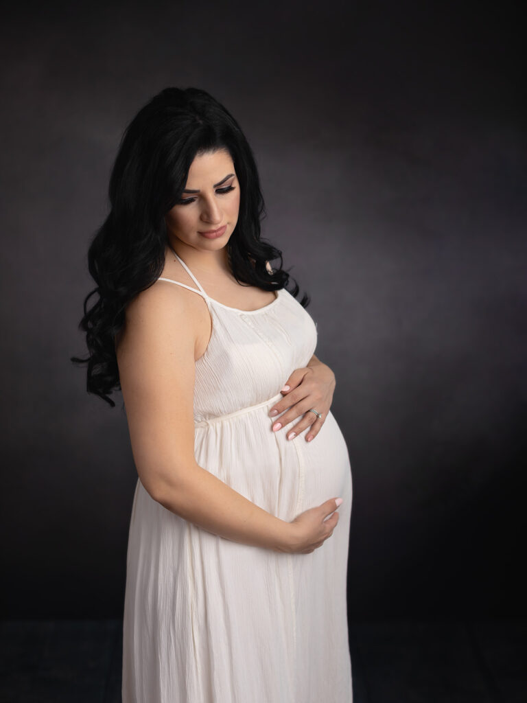 mom to be in white gown cradling her bump