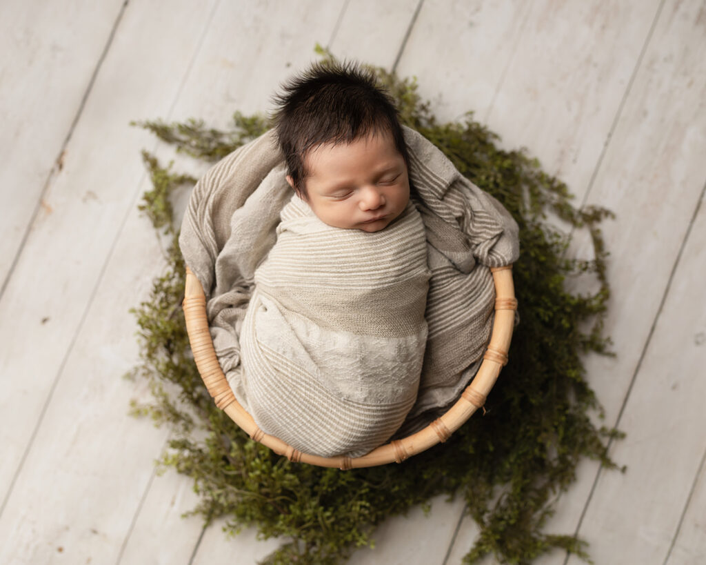 newborn baby wrapped in grey sitting in a basket