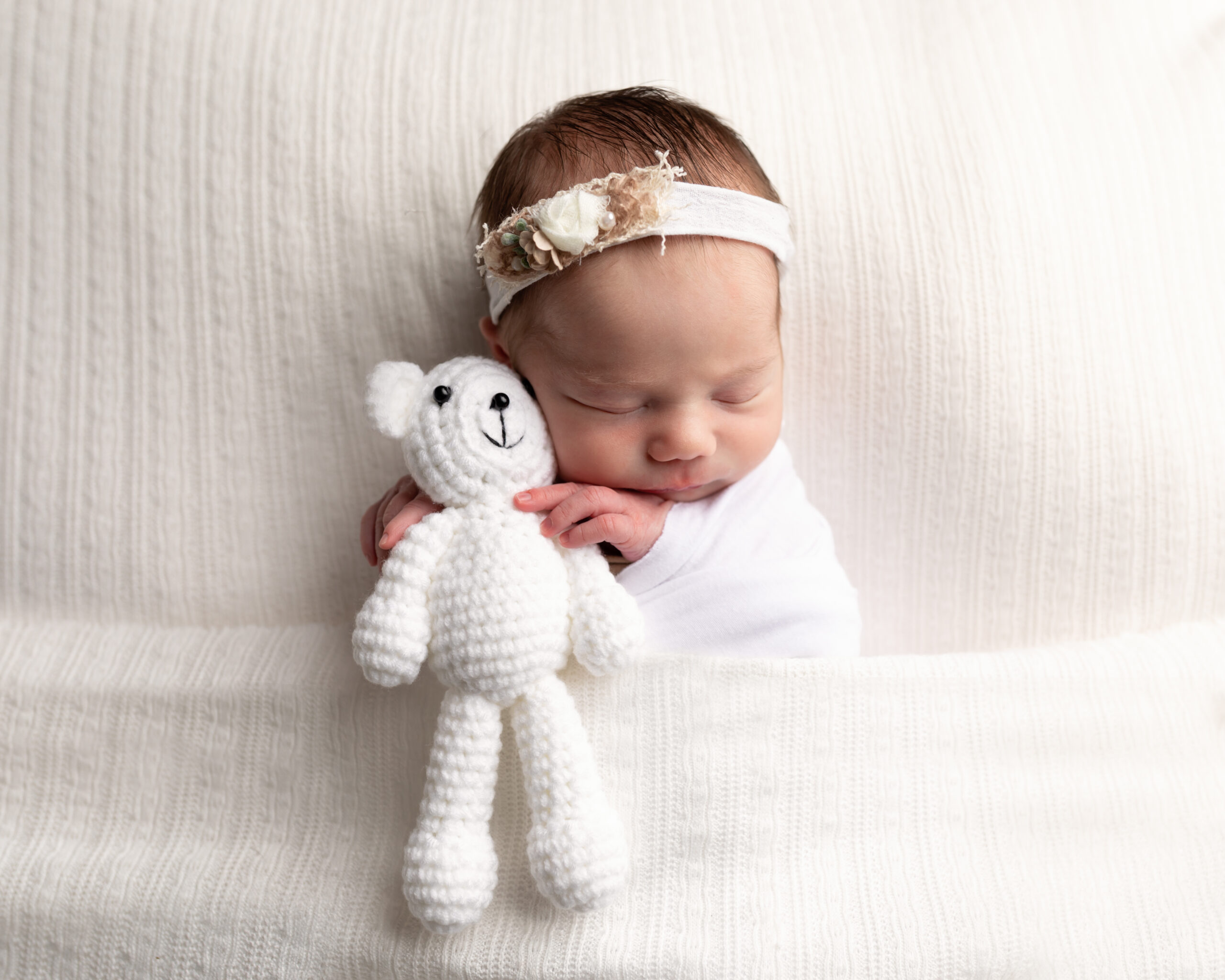 baby wrapped in white holding teddy bear for studio portraits