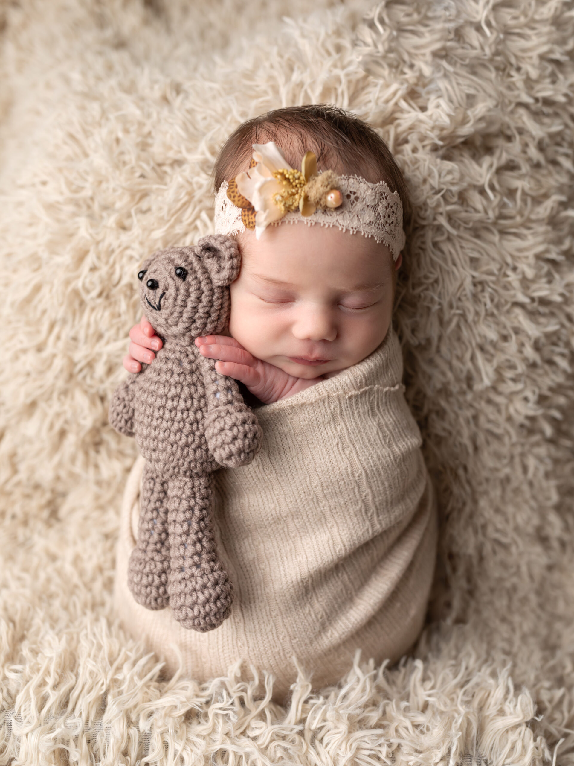 baby wrapped in beige holding teddy bear for newborn portraits