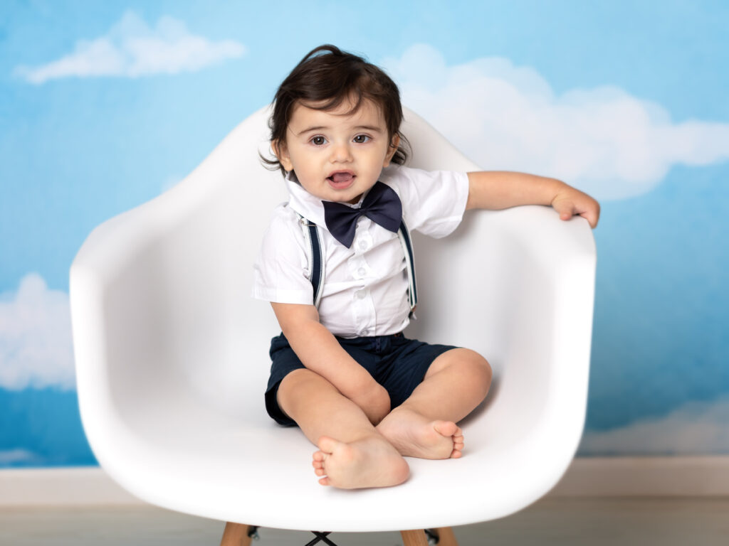 one year old boy sitting in white chair for photoshoot 