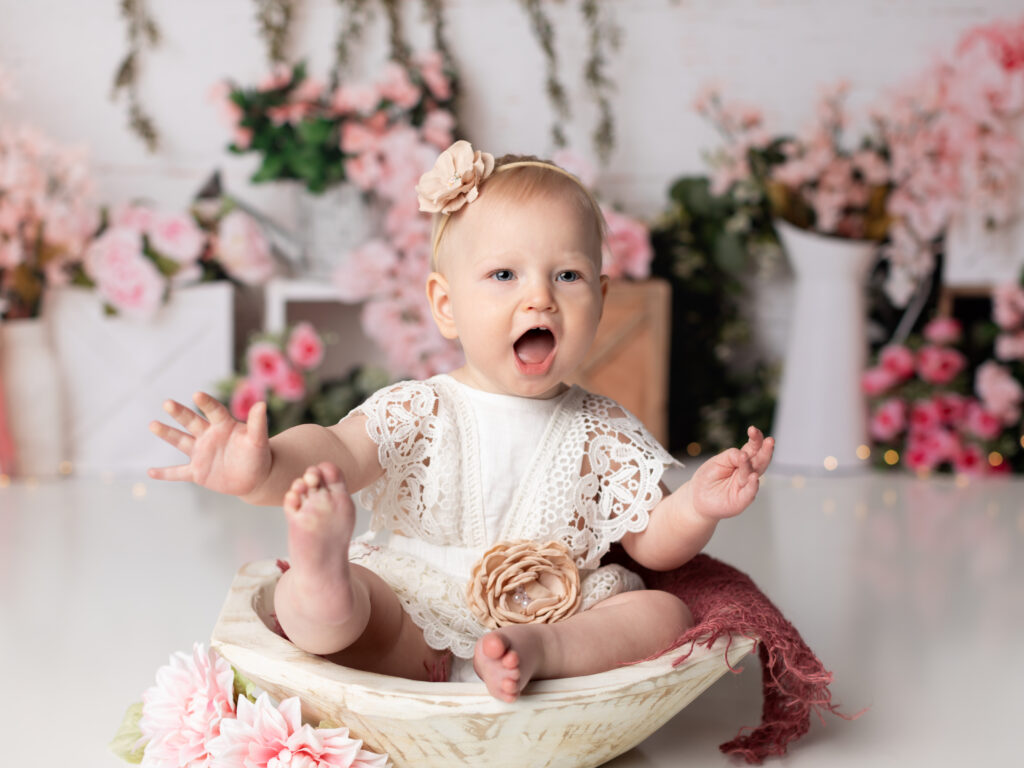 one year old girl sitting in white posing bowl for studio portraits