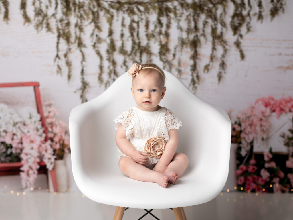 one year old girl sitting in white chair for birthday photoshoot 
