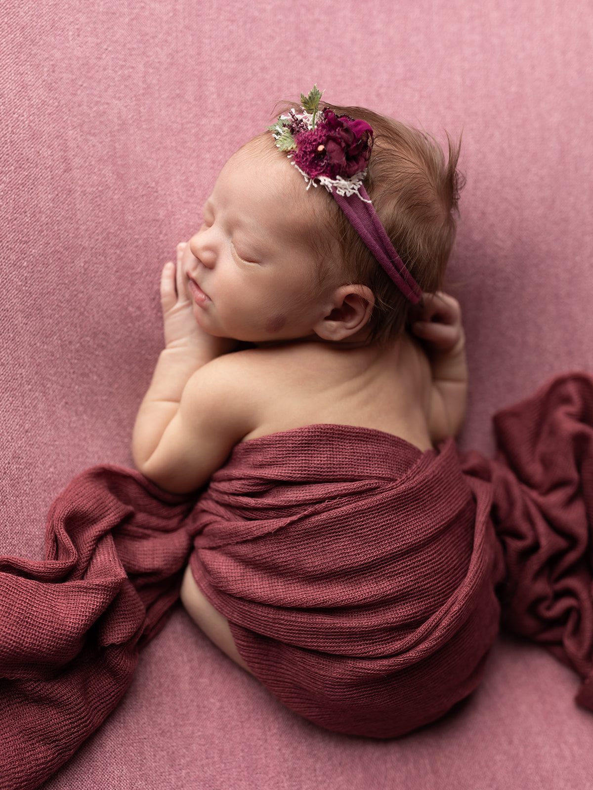 A newborn baby sleeps on her belly wearing a purple flower headband