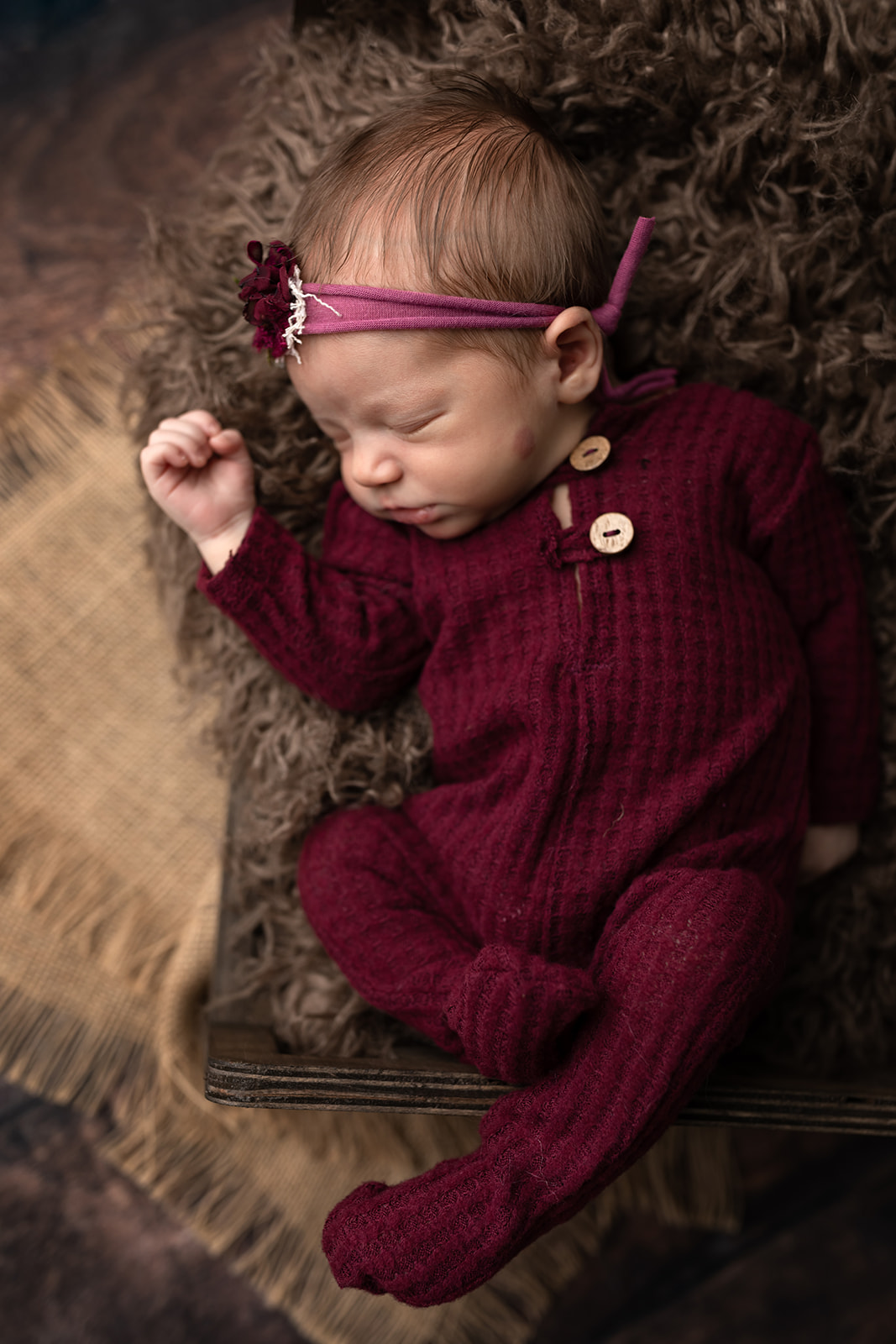 A newborn baby in a purple knit onesie lays on a bed of blankets Little Bellies Cleveland