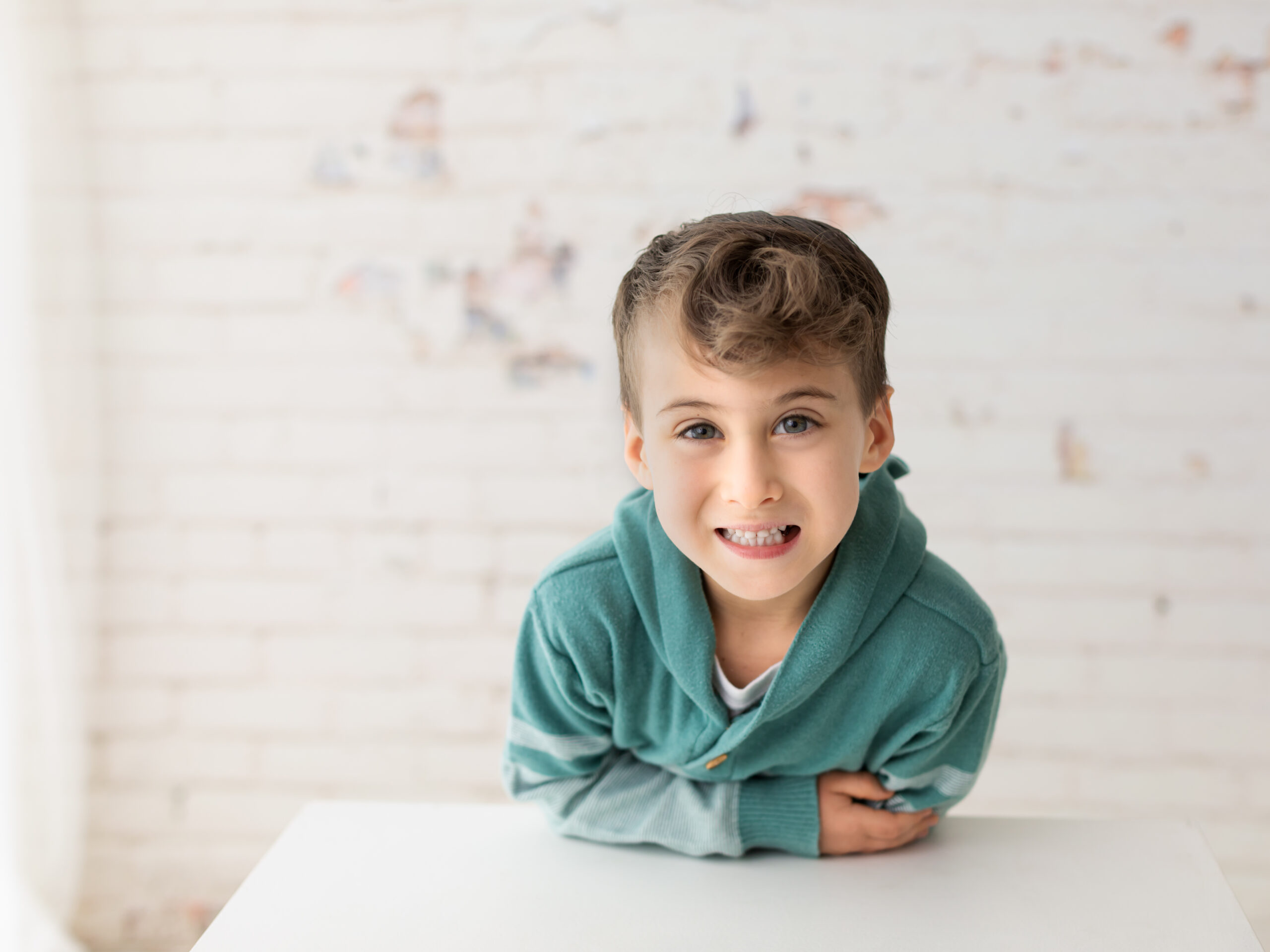 little boy in green hoodie posing for studio portraits with white brick wall pete and polly in brunswick