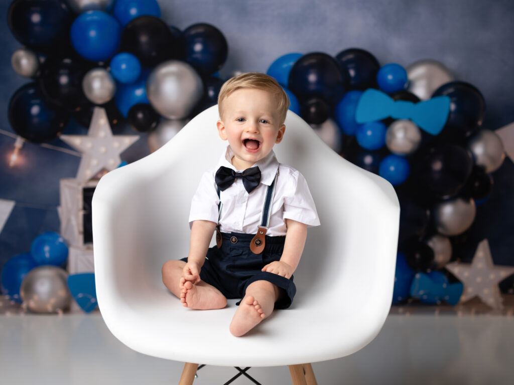 one year old boy sitting in white chair for studio portraits