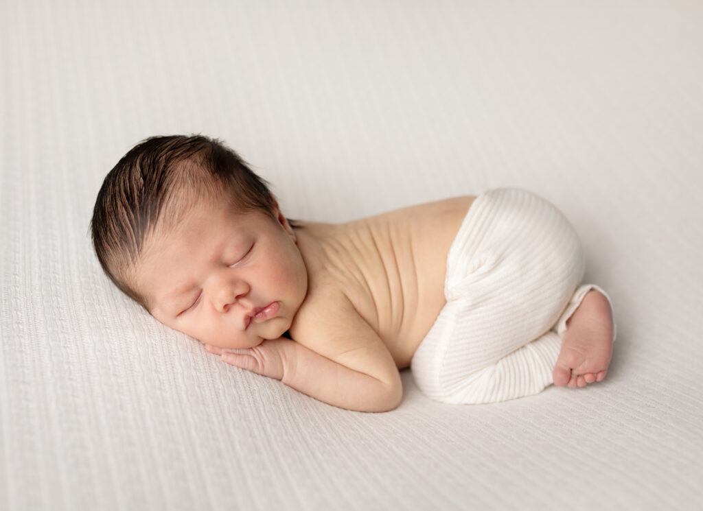 newborn baby boy in white pants posed for newborn studio portraits