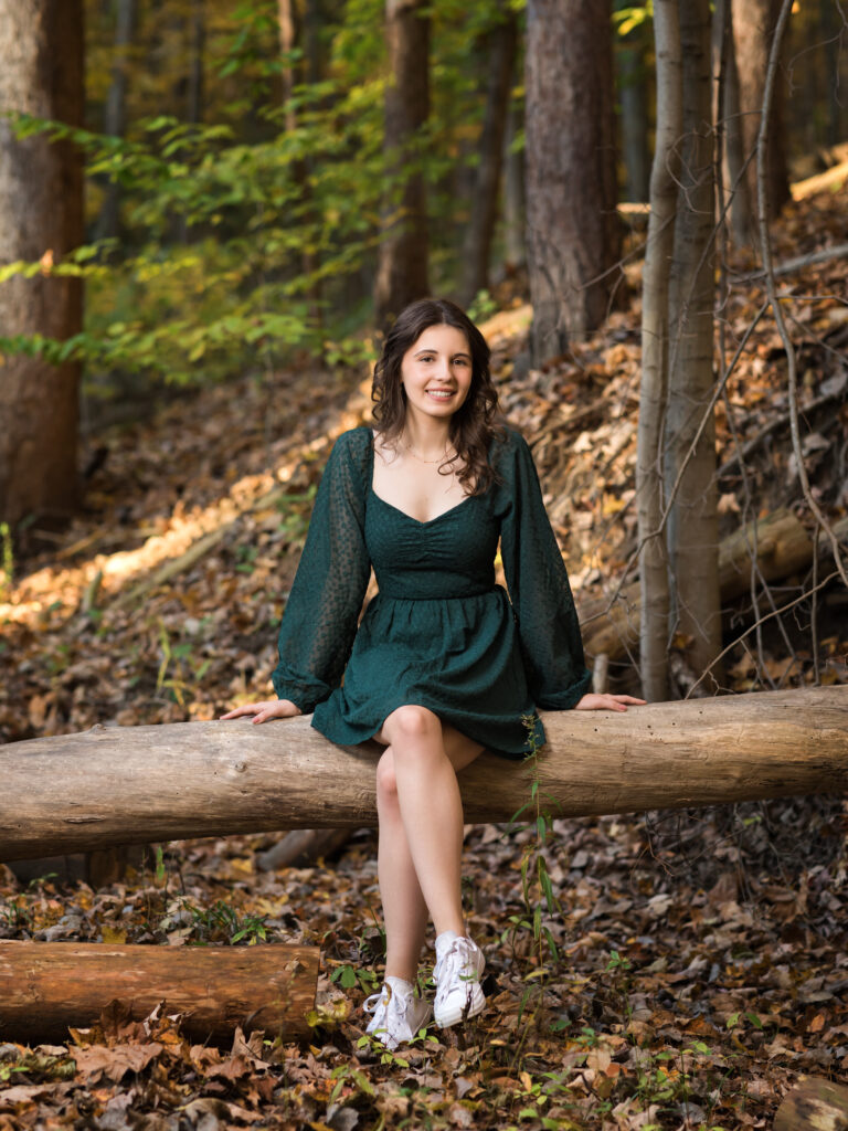 female senior sitting on log in woods for portraits Furnace Run Park