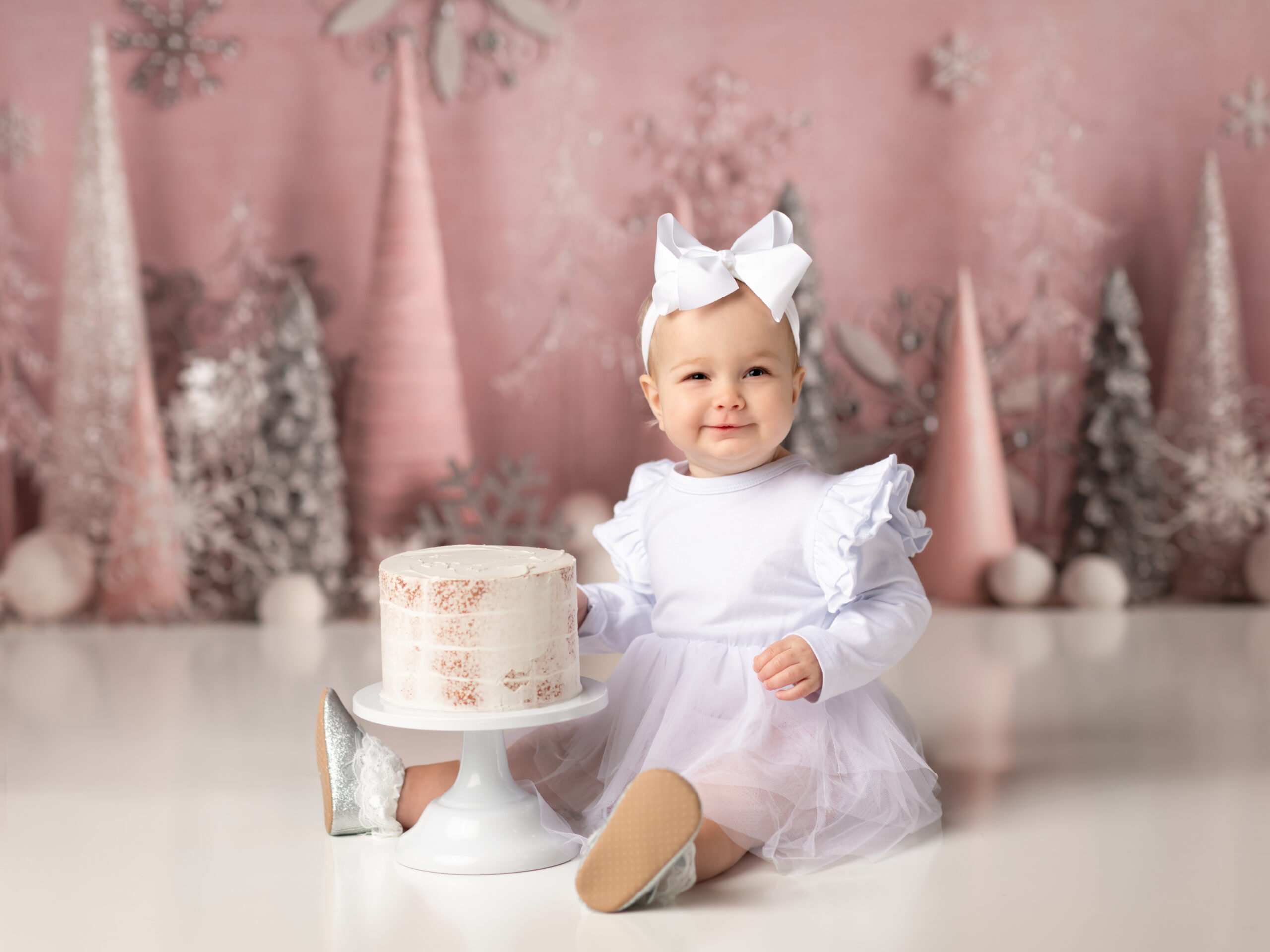 one year old girl in white dress posed for cake smash winter onederland birthday theme