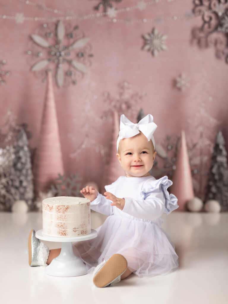 girl in white dress smiling for first birthday photos winter onederland birthday theme