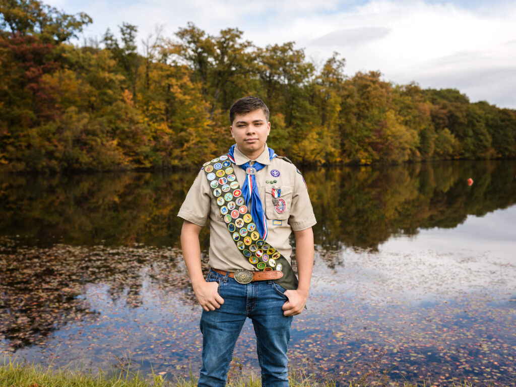 male senior posing by lake with boy scout uniform on for senior photos