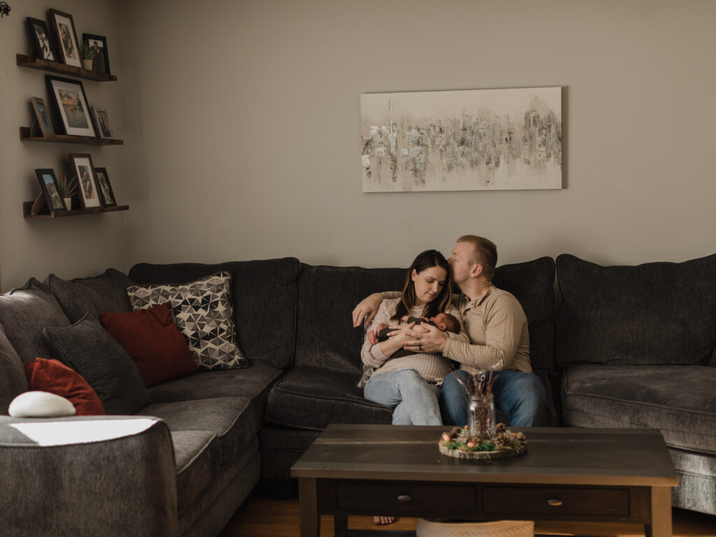 mom and dad sitting in living room with newborn baby boy in for in home photoshoot