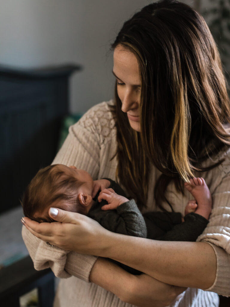 mom holding newborn baby boy in nursery for in home photoshoot