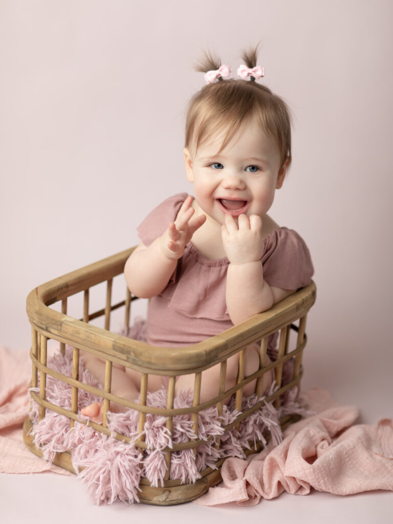 one year old girl in pink sitting in basket for cake cake smash photoshoot