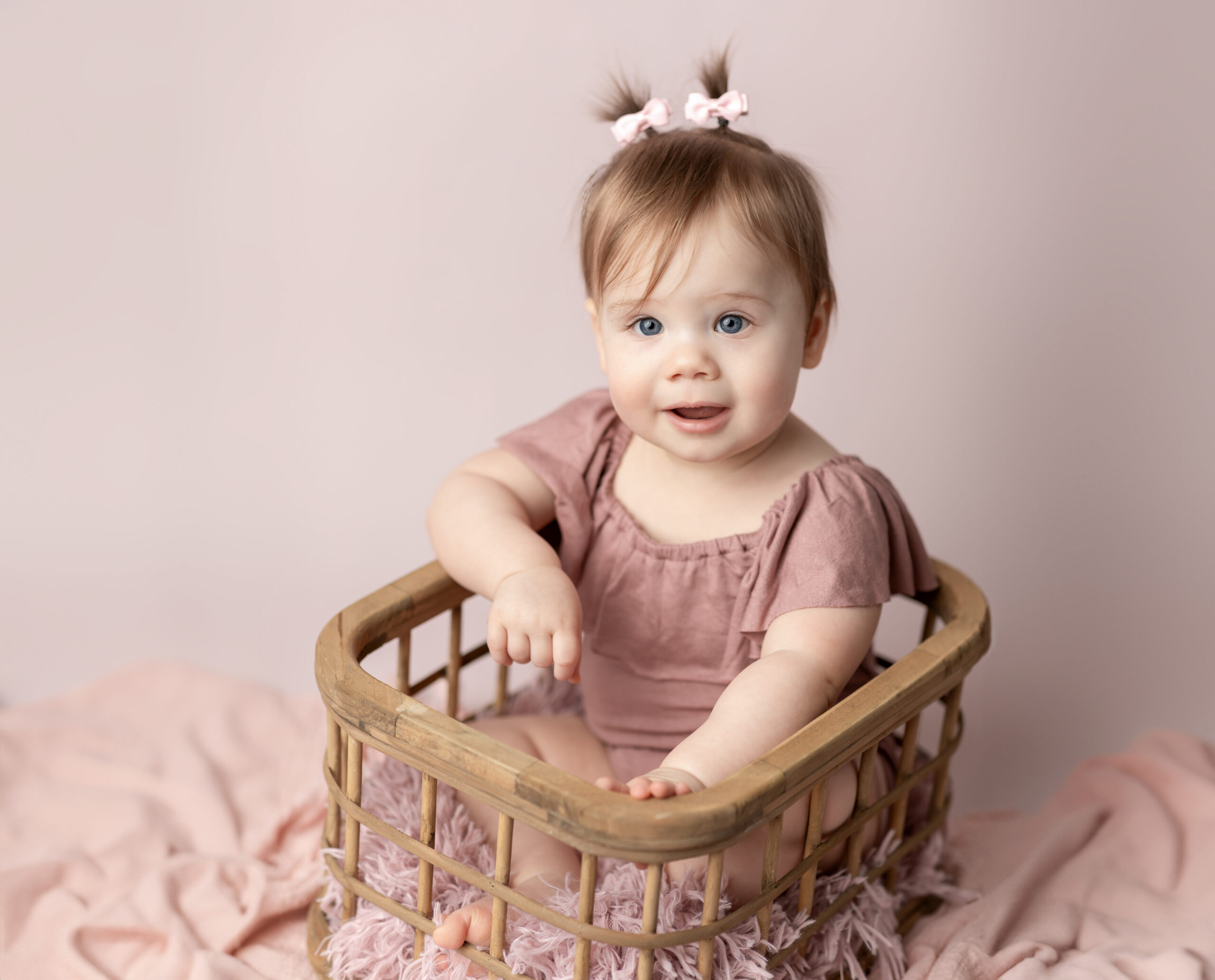 one year old girl in pink sitting in basket for cake smash photoshoot akron ohio photographer