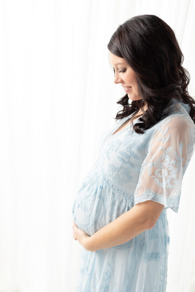 pregnant mother in lace blue dress holding belly for maternity photos