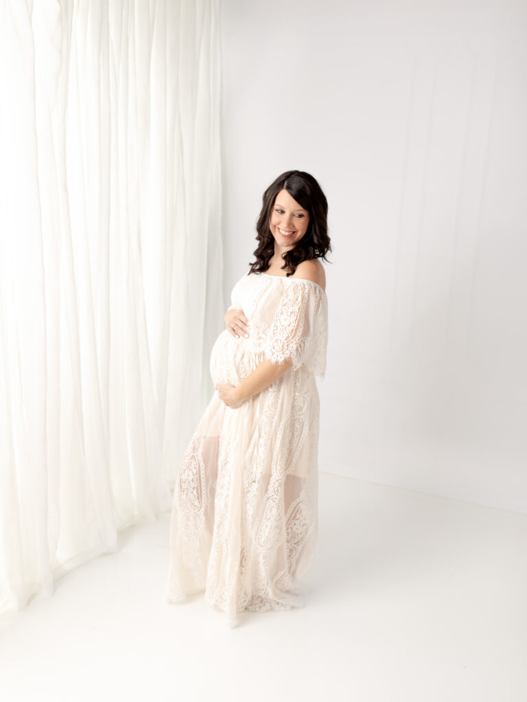 pregnant mom in white lace dress holding baby bump The Womb Wellness Center