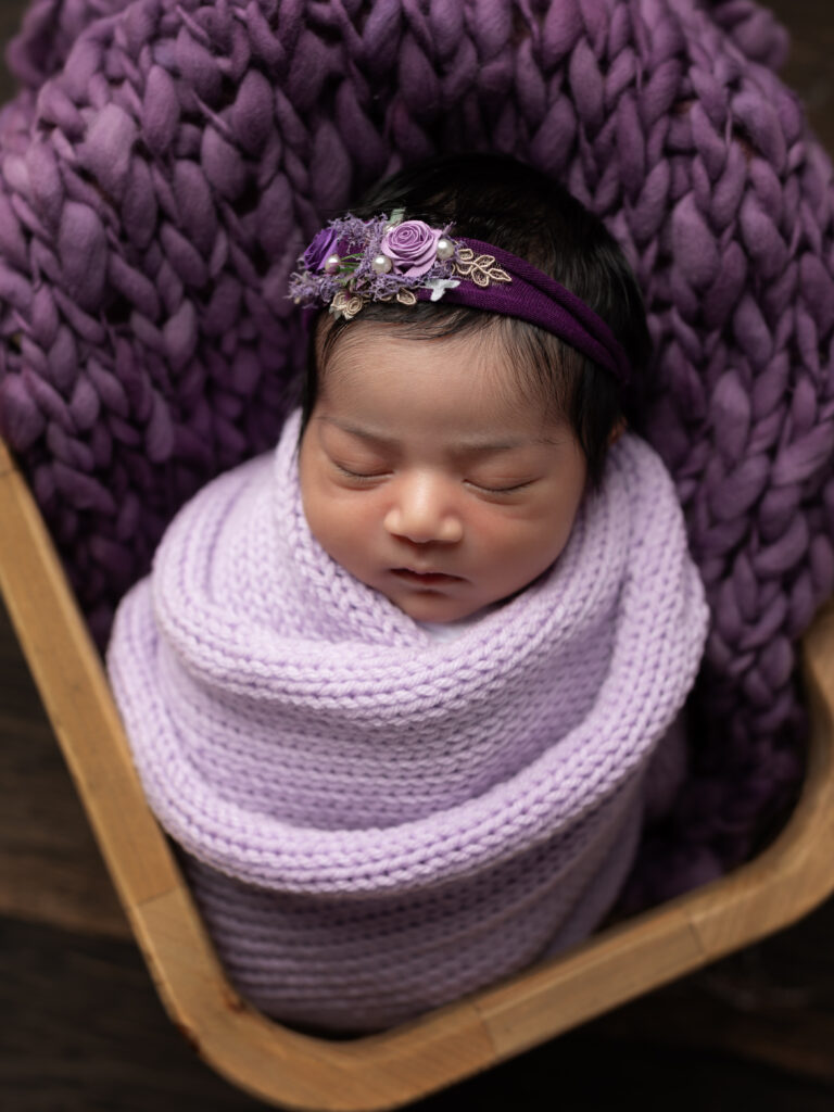 newborn baby girl wrapped in lavender swaddle for studio portraits 