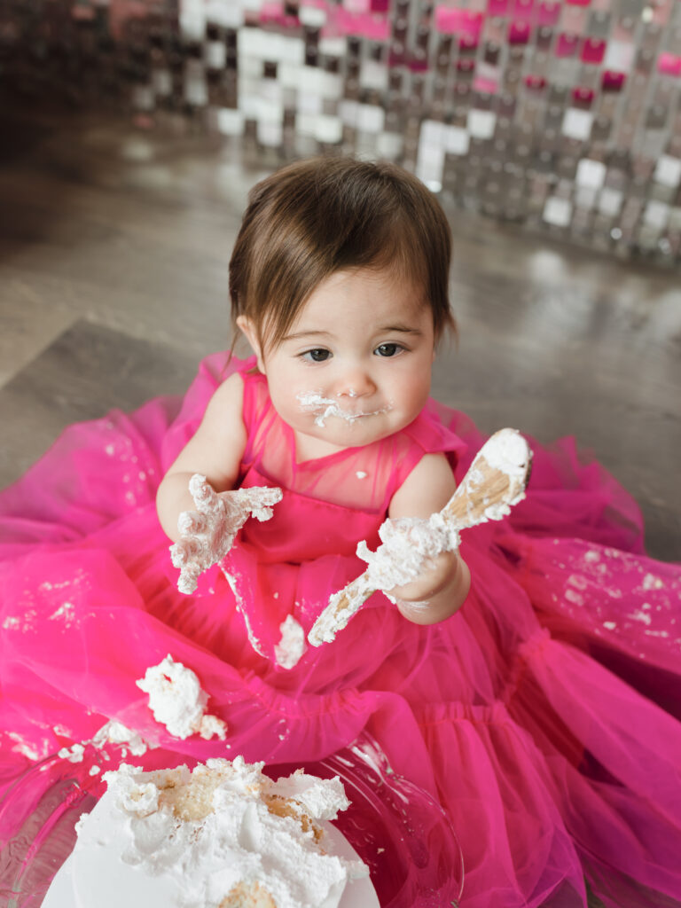 one year old girl eating cake for her first birthday cake smash