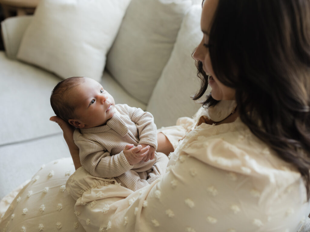 mom holding newborn baby boy on couch for in home lifestyle session