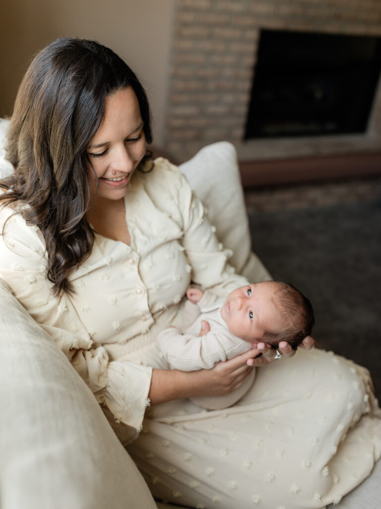 mom holding newborn baby boy on couch for in home newborn session Hatch Boutique