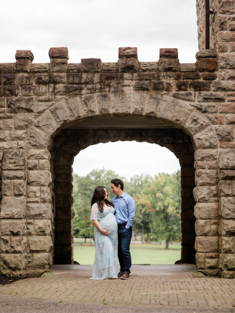 husband and pregnant wife in blue lace dress standing in front of squires castle