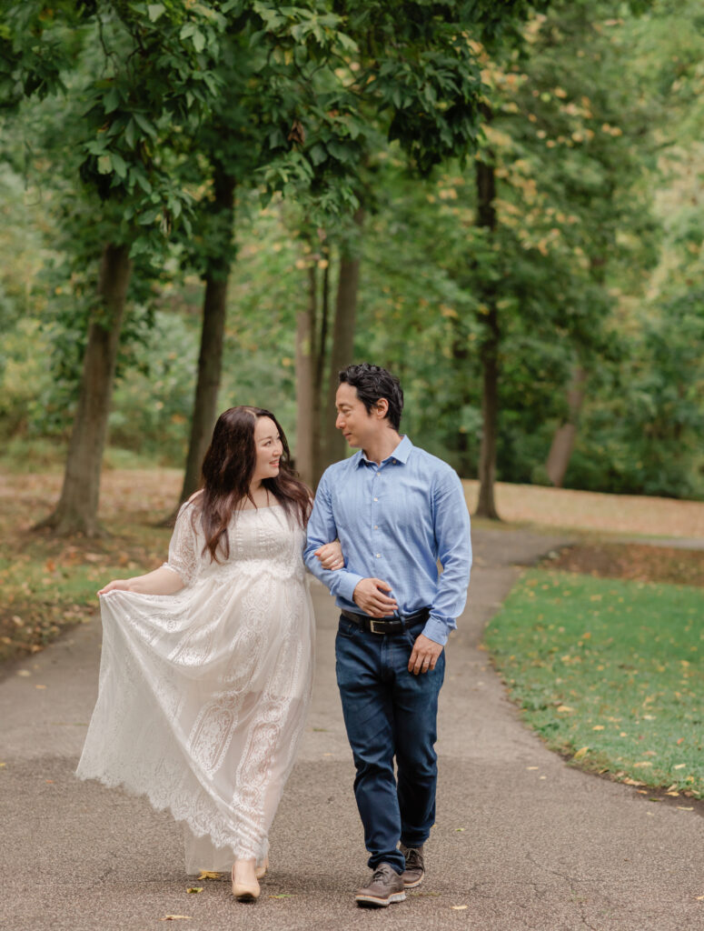 husband and pregnant wife in white lace dress walking along in park Squires Castle