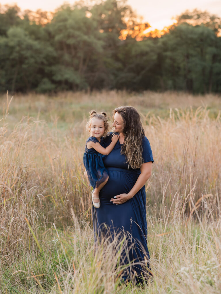 pregnant mother holding daughter for maternity photoshoot in field Ohio maternity photographer