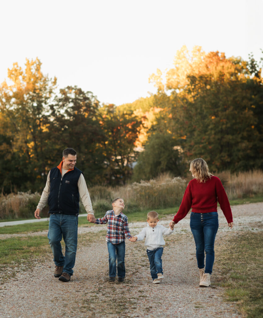 parents and two sons holding handds and walking in park for fall family photos