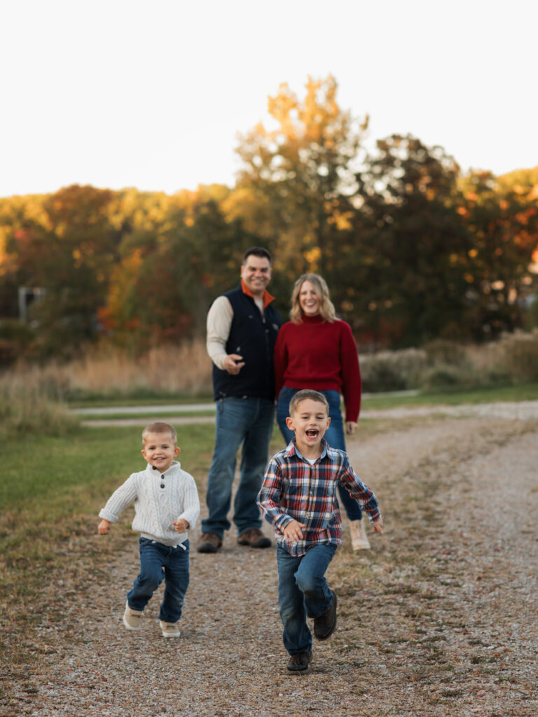 two brothers running from parents in park for fall family photos 