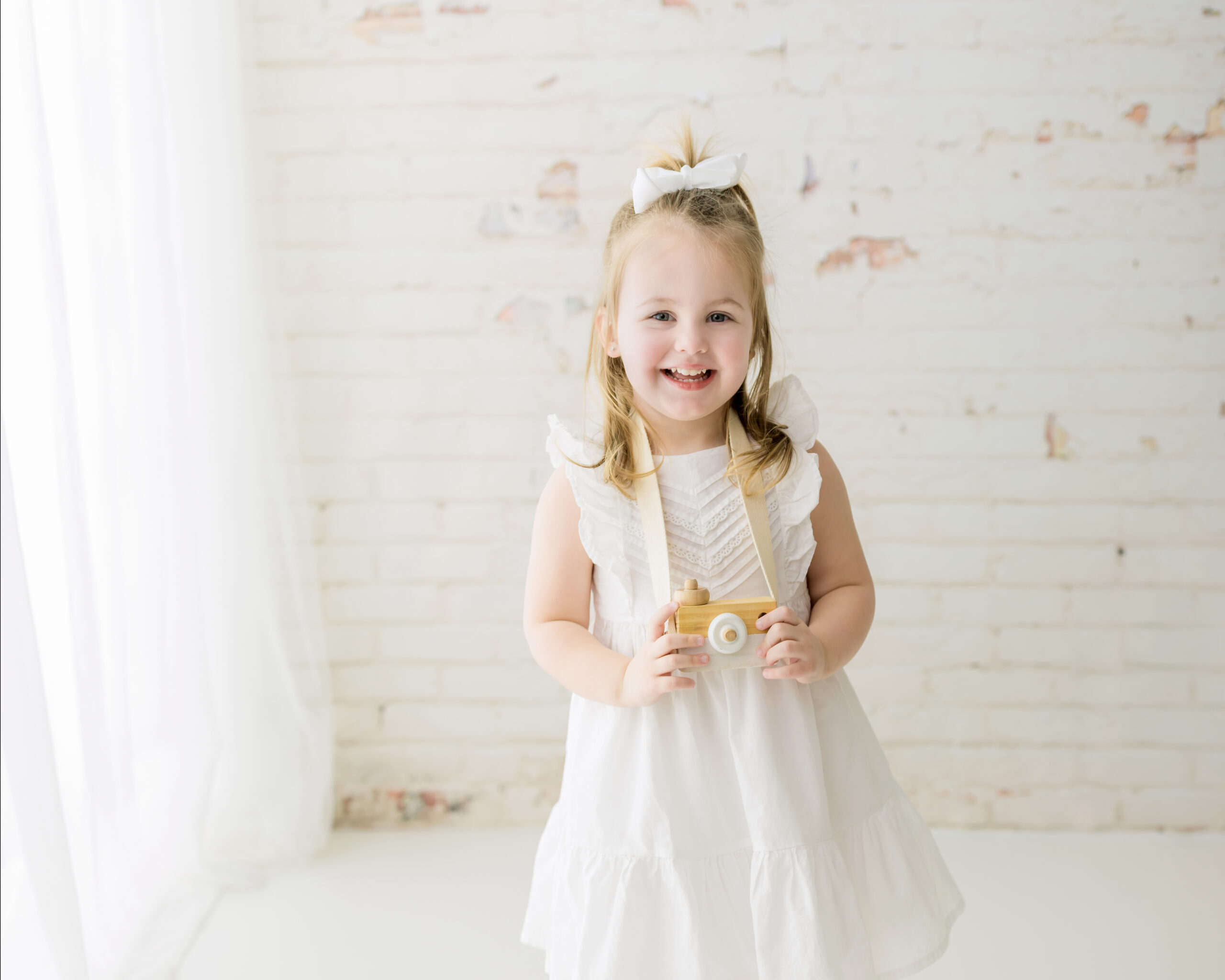 little girl in white dress holding toy camera for studio photoshoot Sweet Kiddles Strongsville