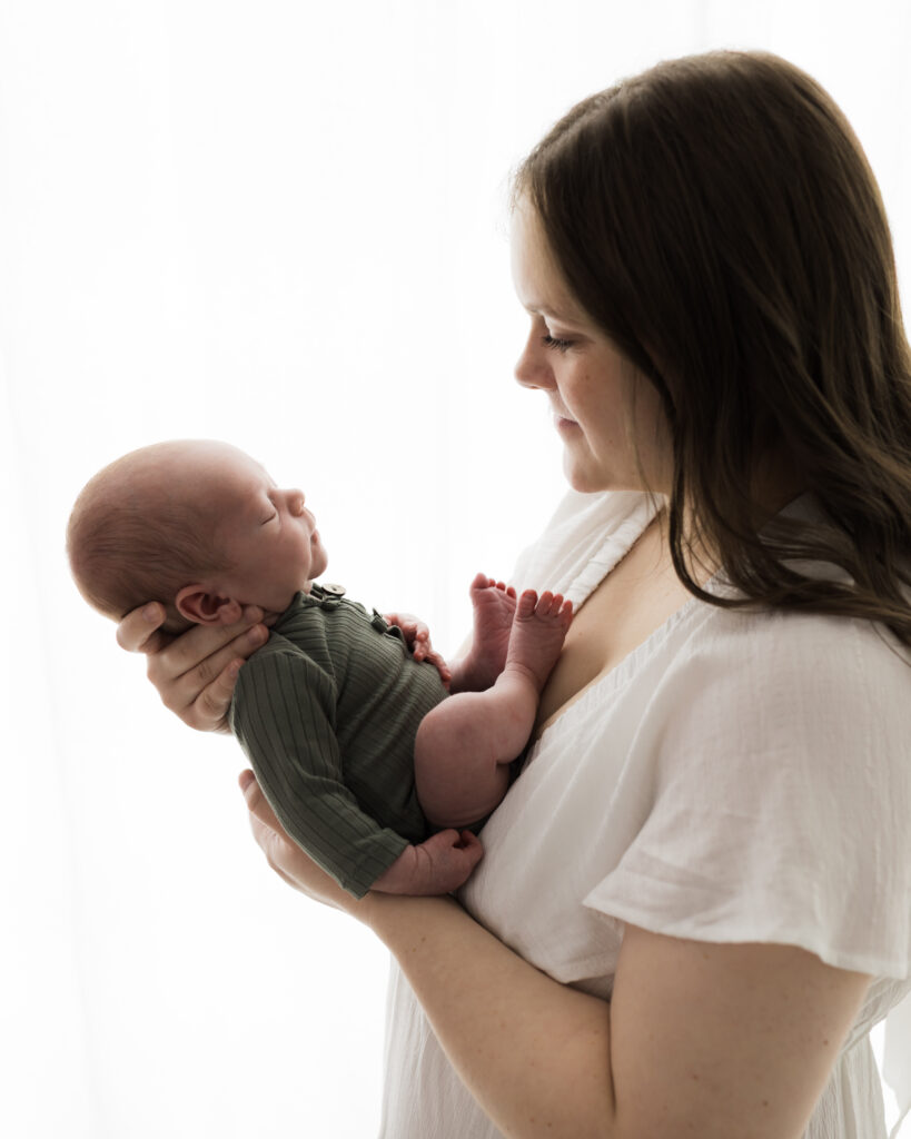 mom in white dress holding newborn son in green onesie for studio portraits Northeast Ohio Newborn Photographer