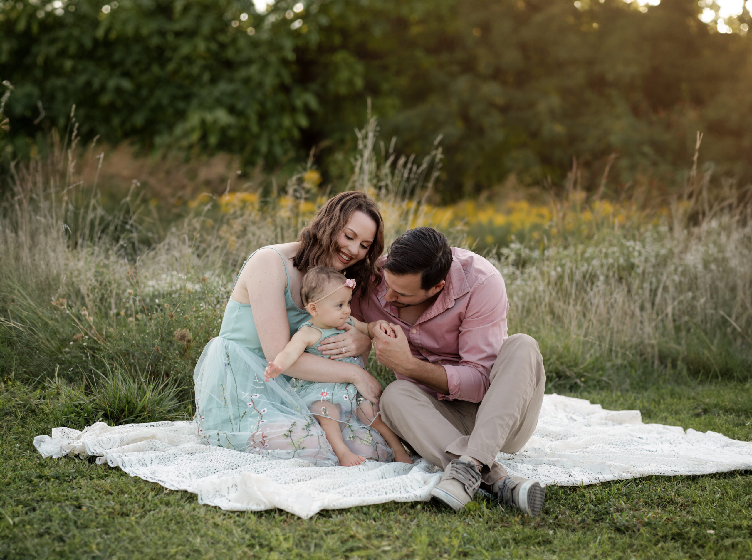 mom and dad sitting on white lace blanket in park with one year old daughter Things To Do In Strongsville