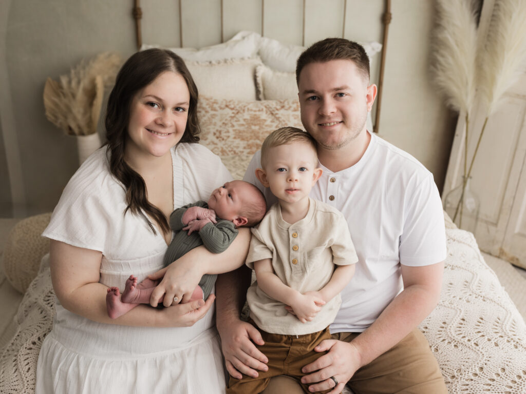 parents dressed in white holding 2 year old son and newborn baby boy for studio portraits 