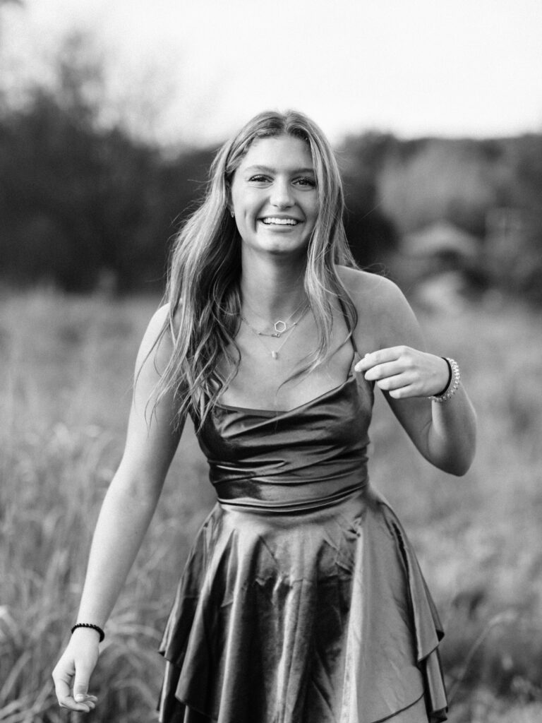 black and white photo of high school senior in dress laughing for senior portraits 