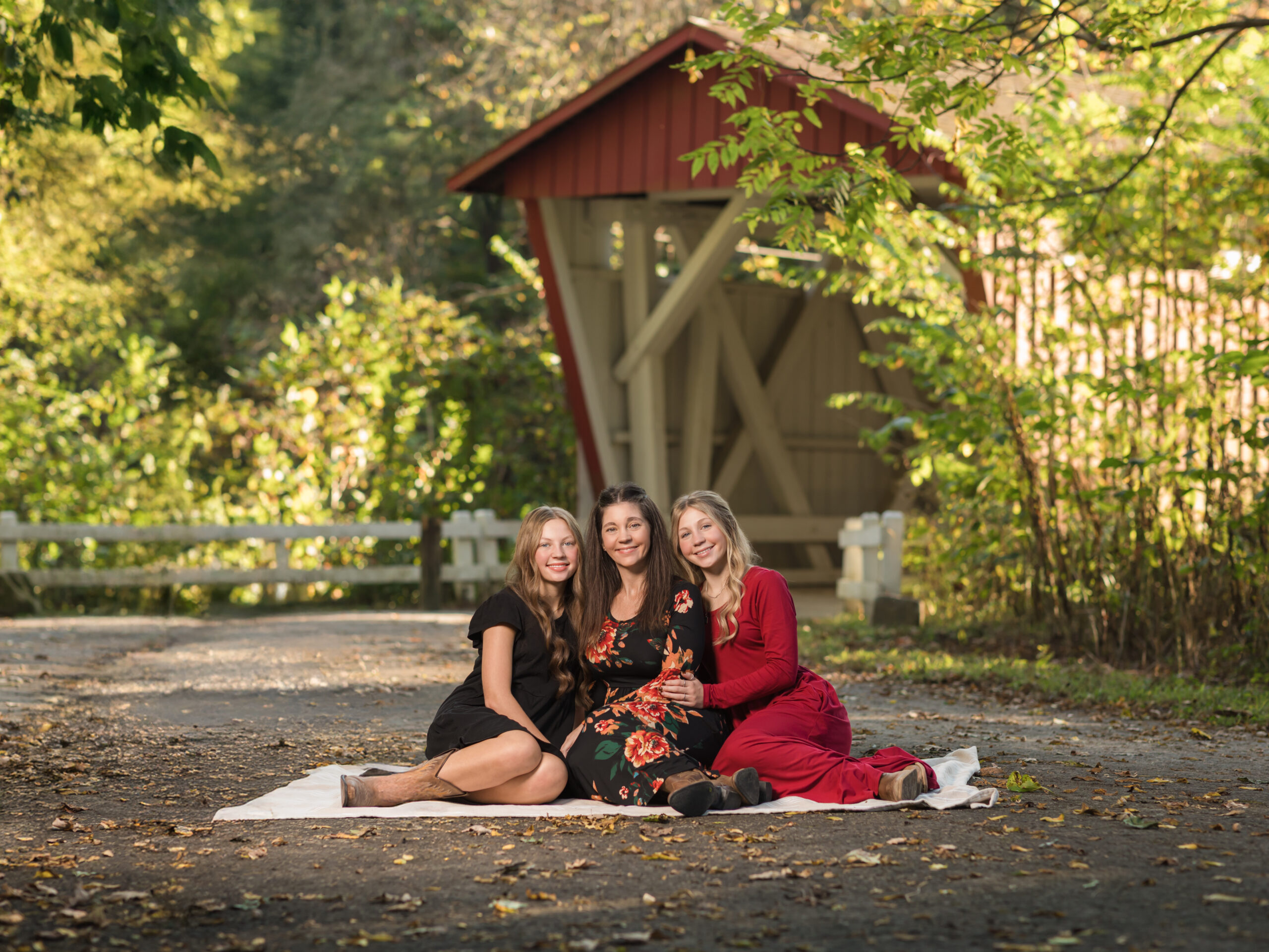 mother and two daughters sitting on blanket in front of bridge for family photos Everett Covered Bridge in Peninsula