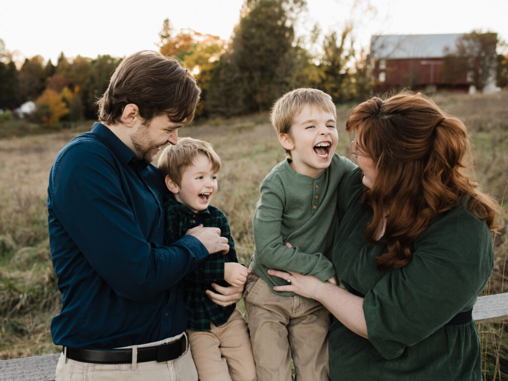 parents hugging and laughing with two sons for fall family photos Allardale Park Medina