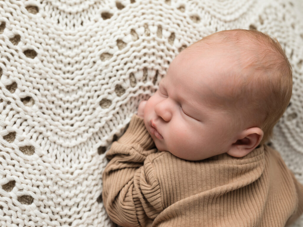 newborn baby boy in tan onesie posed for studio newborn photos Newborn Photography Guide