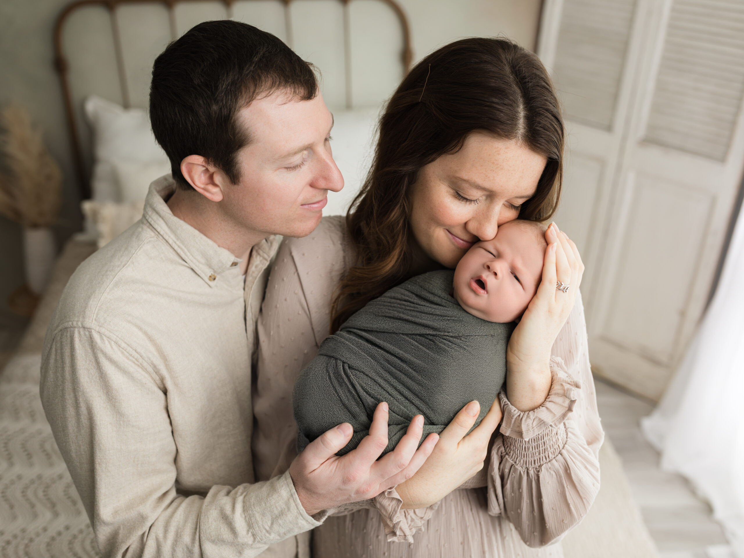 mom and dad holding newborn baby boy swaddled in green wrap Newborn Photography Guide