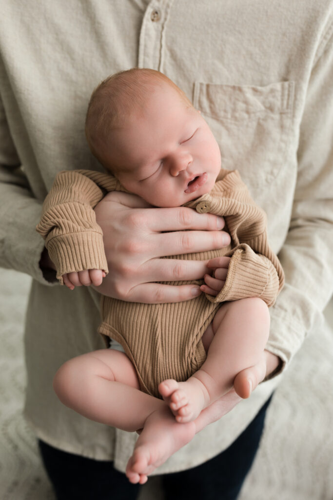 newborn baby boy in tan onesie held by dad