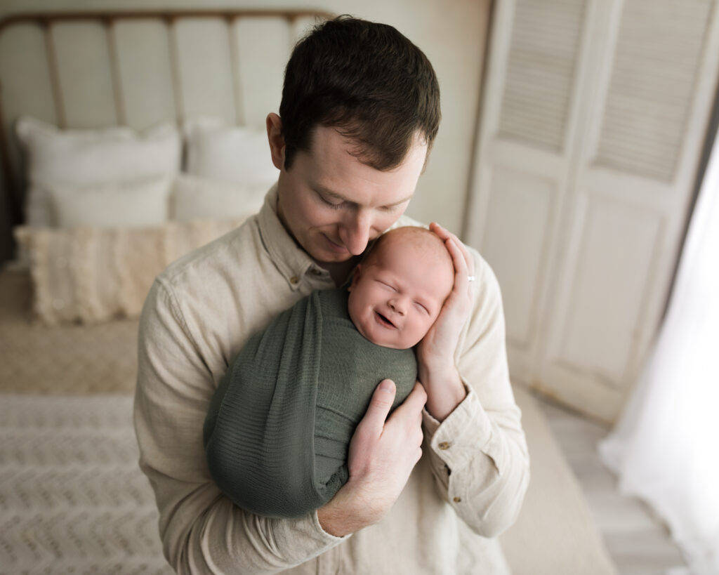 dad holding newborn baby boy swaddled in green wrap Newborn Photography Guide