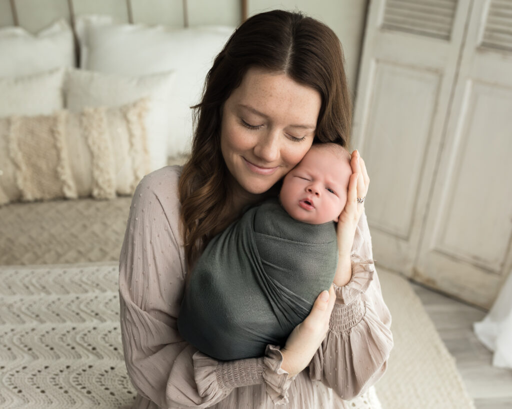 mom holding newborn baby boy swaddled in green wrap Newborn Photography Guide