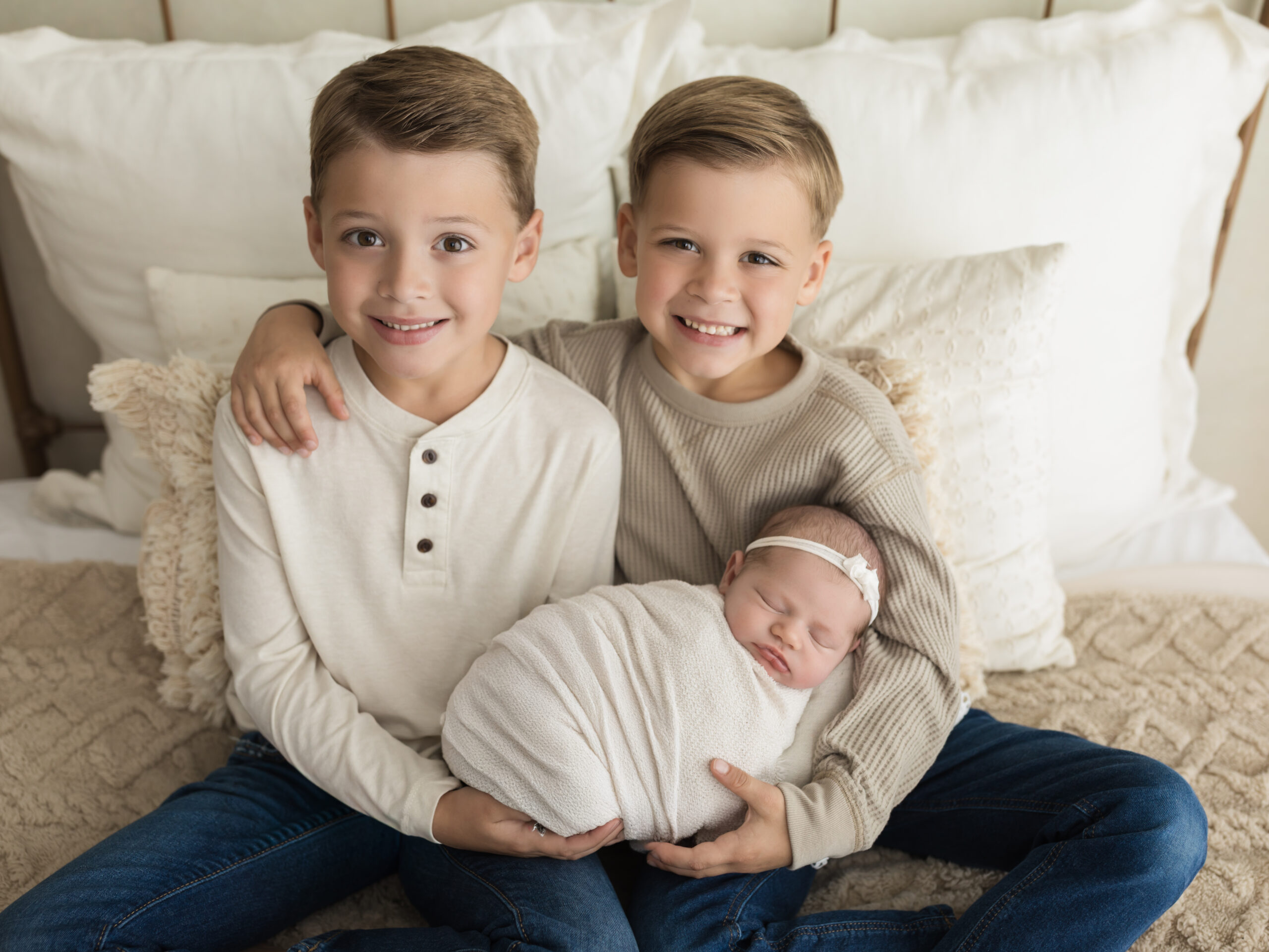 two brothers holding newborn baby sister swaddled in white wrap for studio portraits Pottery Barn Cleveland