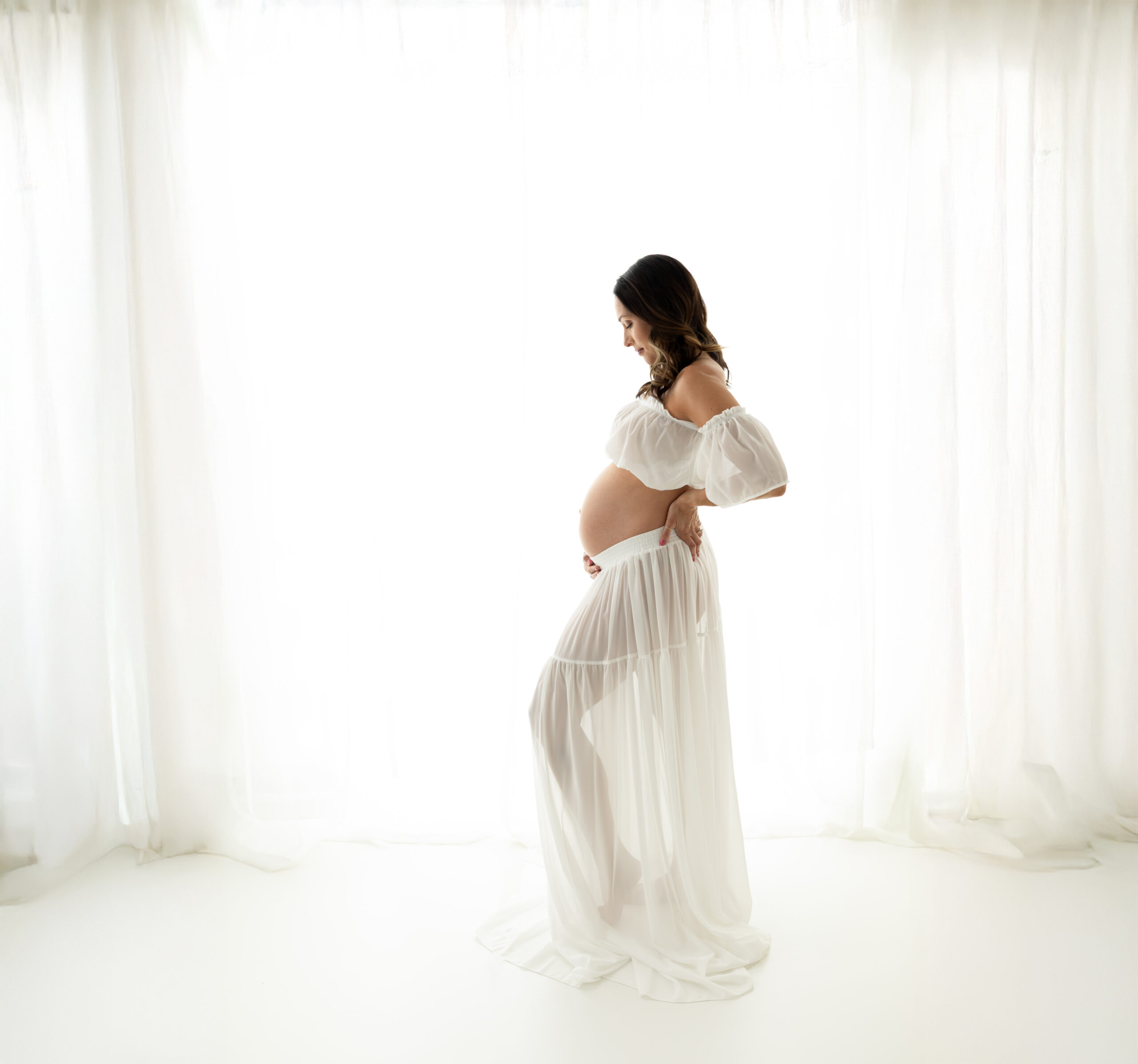 pregnant mother in white two piece dress holding baby bump Prenatal Yoga Lakewood